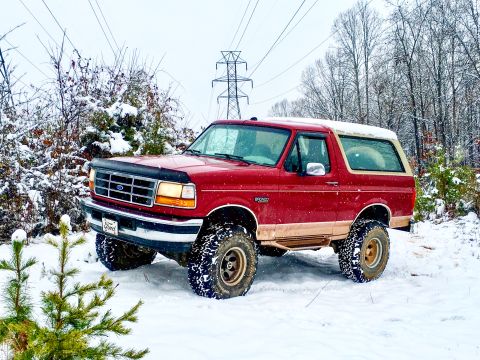 1995 Ford Bronco - A red 1995 Ford Bronco navigates a snowy terrain, its off-road capabilities.