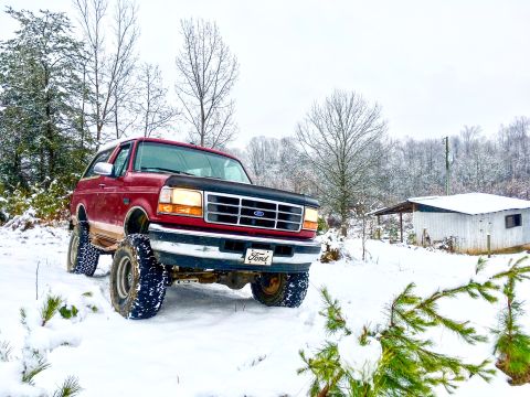 1995 Ford Bronco - Red 1995 Ford Bronco sits in the snow, surrounded by bare trees and a white building.