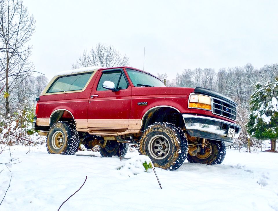 Red 1995 Ford Bronco with lifted suspension and off-road tires in the snow.