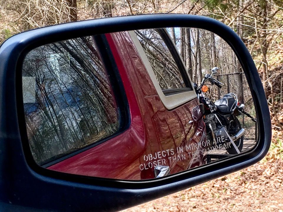 Reflection of a motorcycle and text in a side-view mirror of a red vehicle.