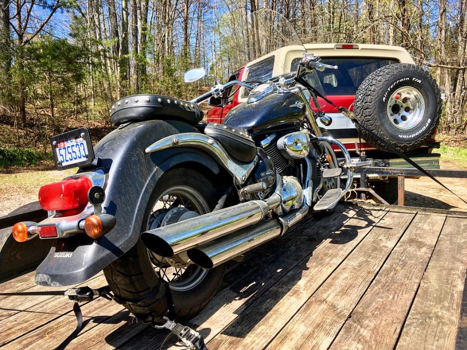 Black Suzuki motorcycle on a trailer, red and tan Ford Bronco in background.