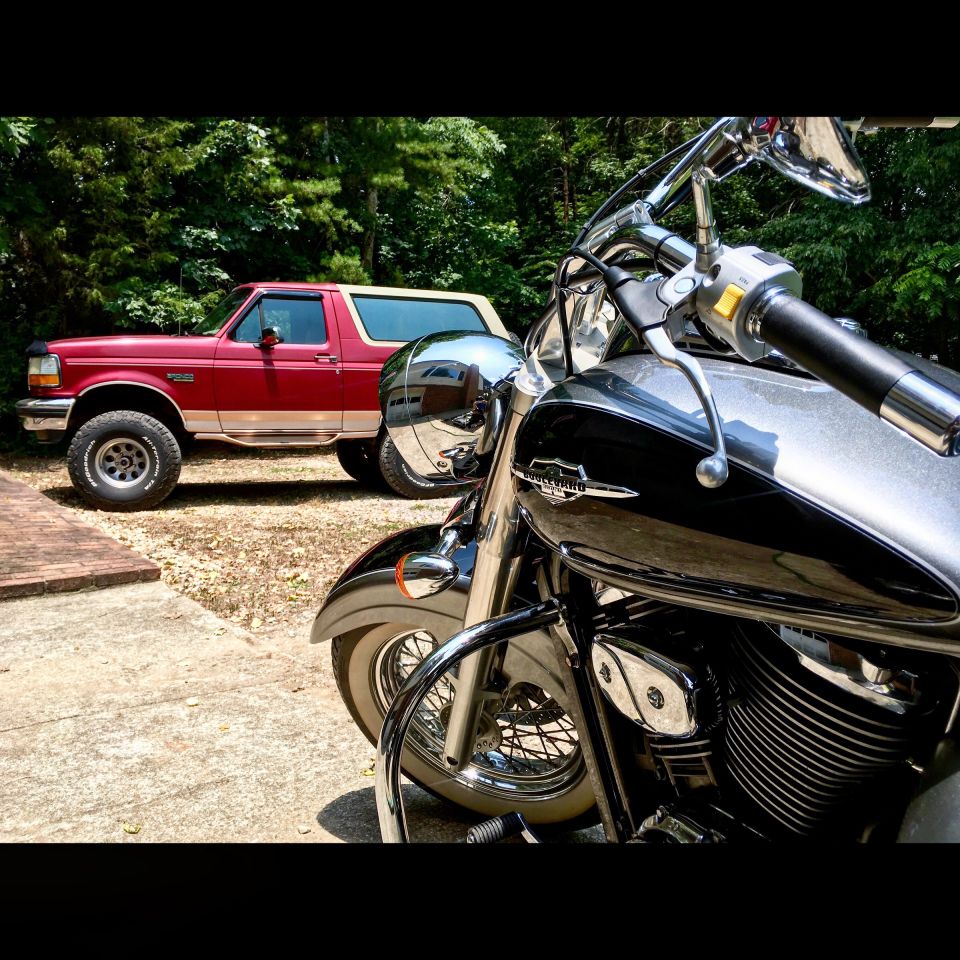 Red and tan Ford Bronco parked next to a black and silver motorcycle.