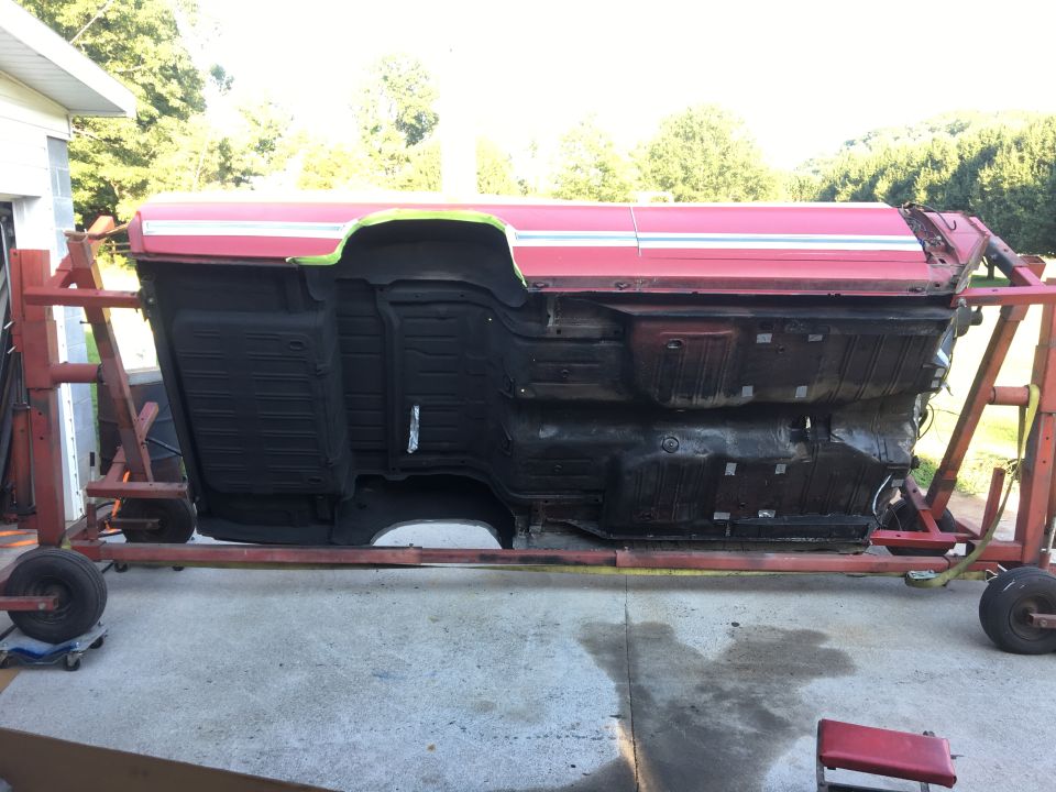 Underside of a red classic car body on a rotisserie stand, black undercarriage.