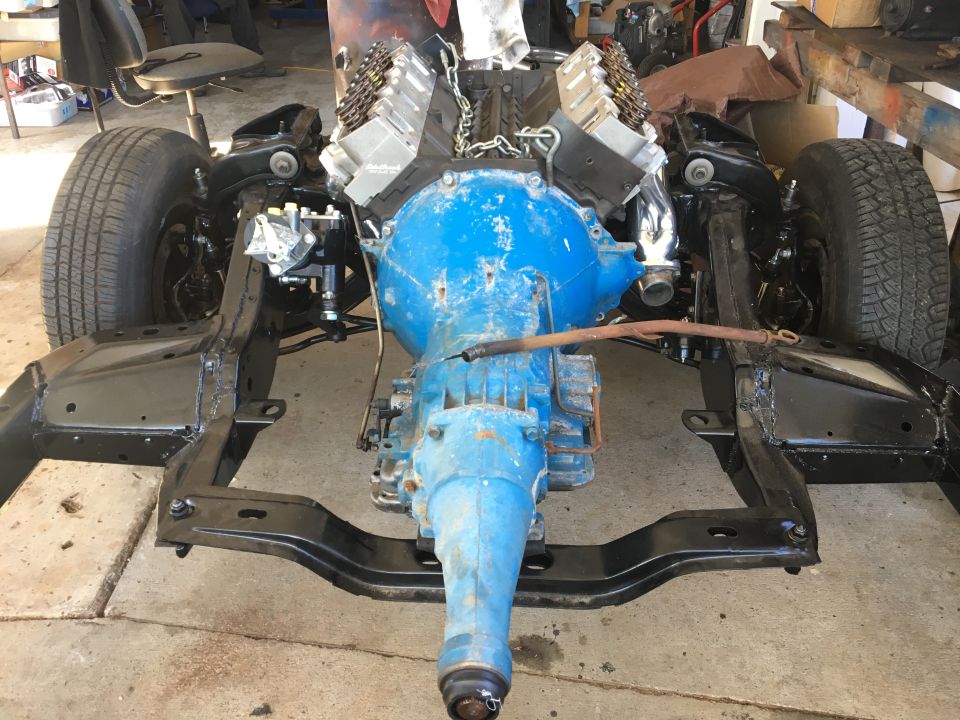 Classic car chassis with blue engine and transmission assembly installed.