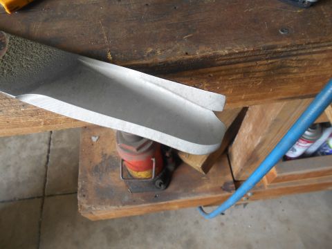 1992 Ford Bronco - A close-up view of a sharpened lawnmower blade resting on a wooden workbench. A red and yellow hydraulic jack is visible underneath the bla…
