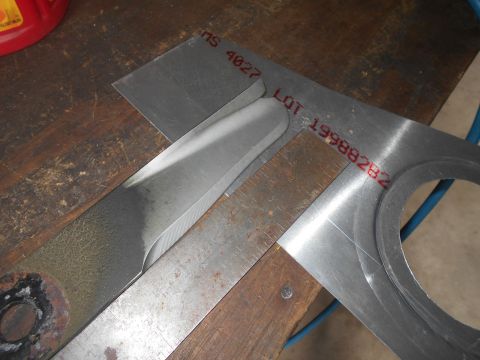 1992 Ford Bronco - A metal lawn mower blade is being measured with a square and ruler on a wooden workbench. A metal template with red lettering is also visib…