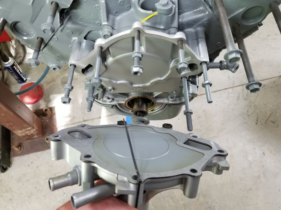 New aluminum water pump being fitted to the timing cover of a rebuilt gray-painted V8 engine