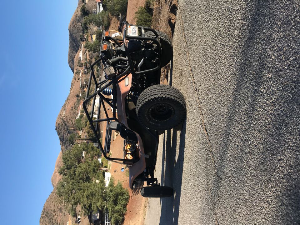 Brown dune buggy with roll cage parked on a road with hills behind