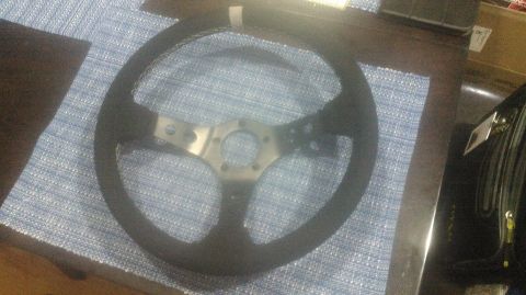 1992 Ford Bronco - A black aftermarket steering wheel with a silver hub is shown from a slightly elevated angle, resting on a blue textured mat. The steering…