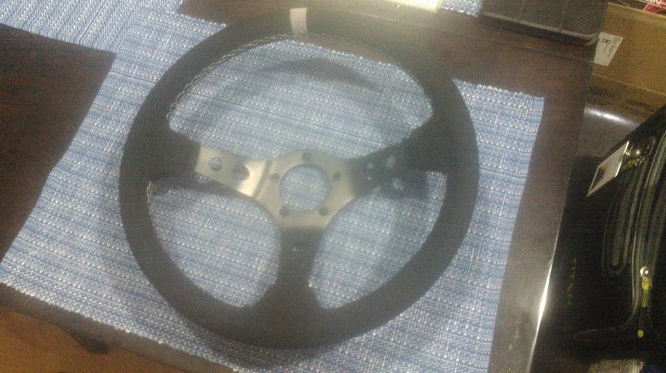 Black aftermarket steering wheel with silver hub and white stitching.