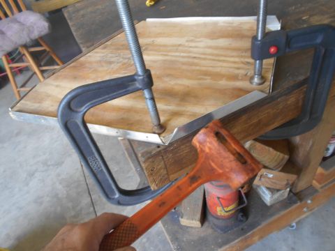 1992 Ford Bronco - A hand is holding an orange-handled mallet, about to strike a piece of metal that is clamped to a wooden surface. A metal C-clamp is also v…
