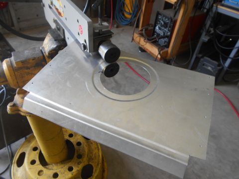 1992 Ford Bronco - A metal sheet with a circular cutout is being shaped by a metal roller machine. The machine is mounted on a yellow industrial stand.