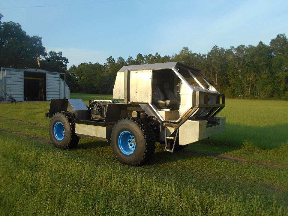 Custom four-wheeled vehicle with silver body and blue rims in a grassy field.