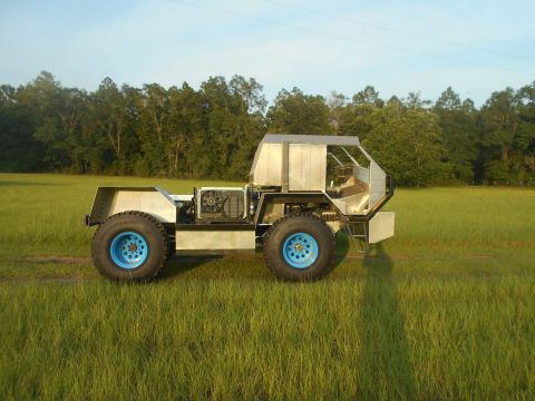1992 Ford Bronco - A custom-built, four-wheeled vehicle with large blue-rimmed tires sits in a grassy field. The vehicle has an exposed engine bay with a visi…