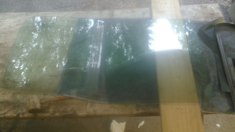 Curved green tinted glass reflecting trees and sunlight, resting on a wooden surface.