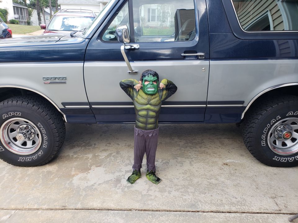 Child dressed as the Hulk in front of a blue and silver Ford Bronco