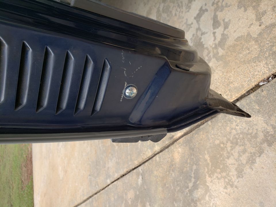 Dark blue vehicle door with vents and a screw, resting on concrete.