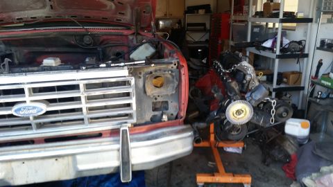 1981 Ford Bronco - A red Ford truck with its hood open is parked in a garage next to a disassembled engine on an engine stand. The front grille and bumper are…