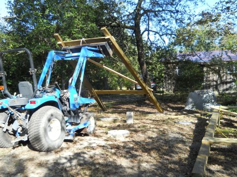 1992 Ford Bronco - A blue tractor with a front loader is parked next to a wooden structure under construction. The tractor is positioned in a dirt lot with tr…