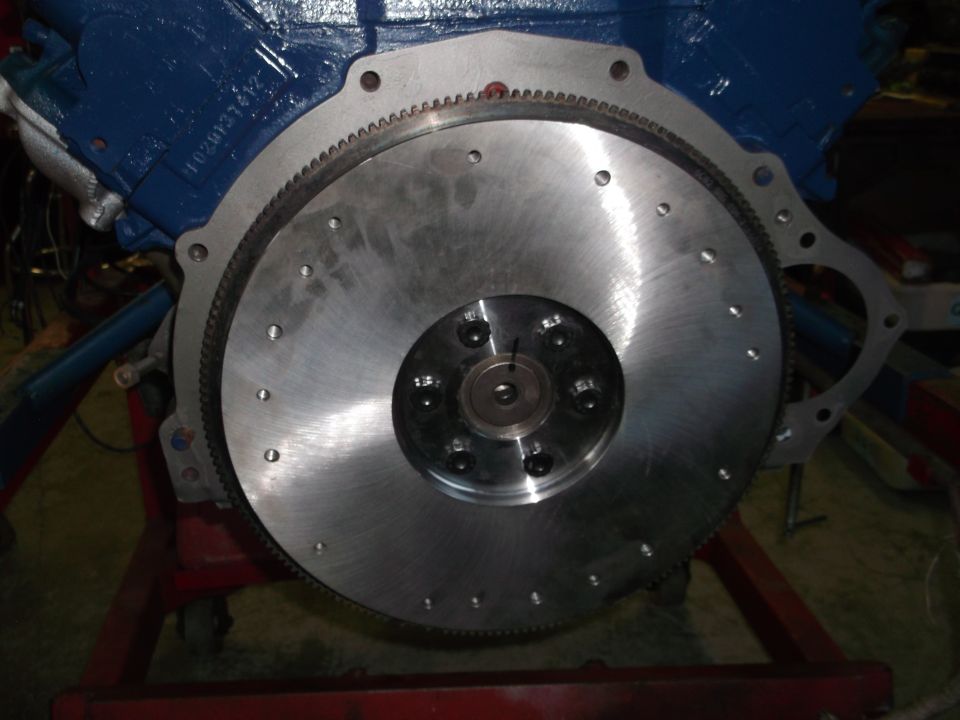 Close-up of a flywheel attached to a blue engine on a stand.