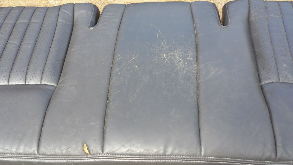Close-up of a worn dark gray leather car seat with stitching and perforations.