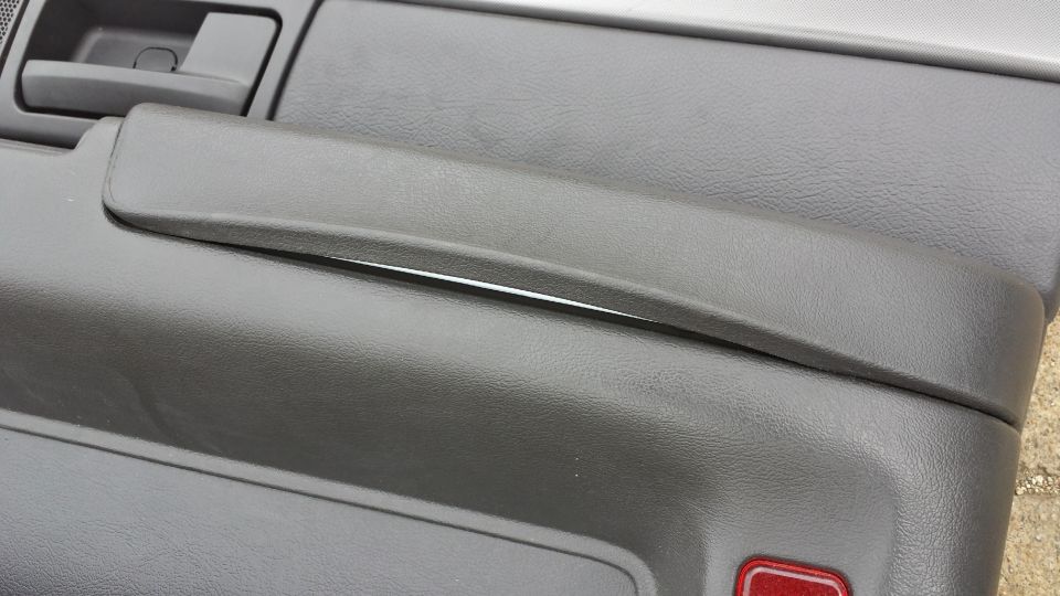 Gray plastic car door panel with a separated armrest and a red reflector.