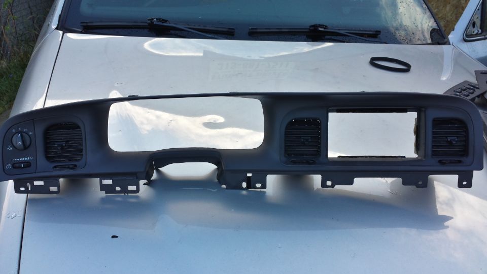 Dark gray dashboard trim piece with vents and gauge cutouts on a silver car hood.