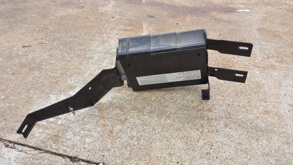 Black electronic control module with metal bracket on concrete.