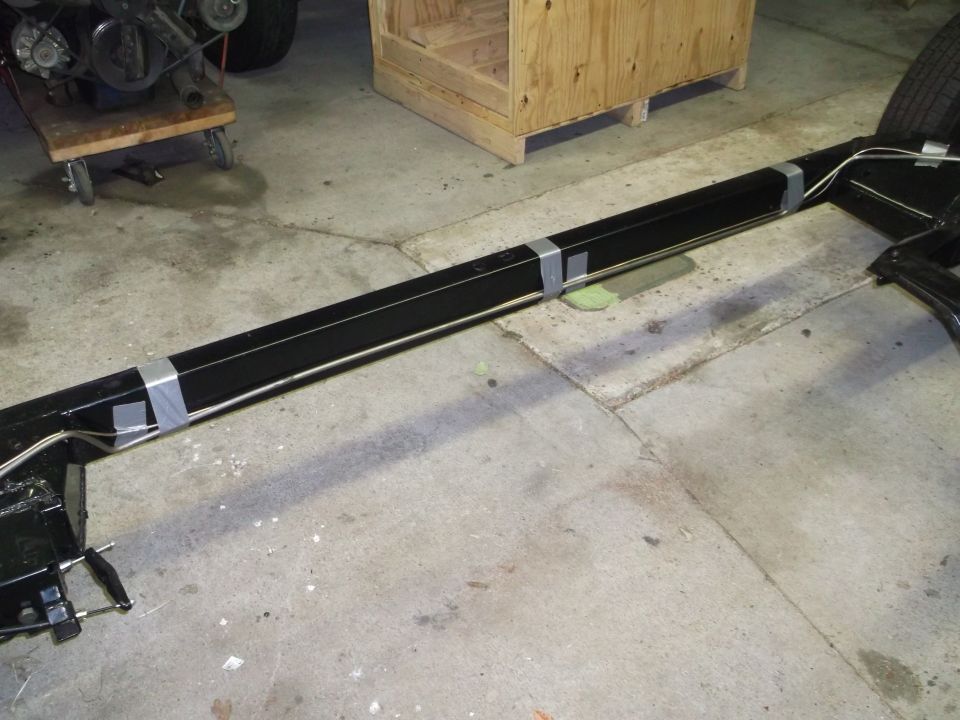 Black vehicle frame with silver tube secured by gray tape on concrete floor.