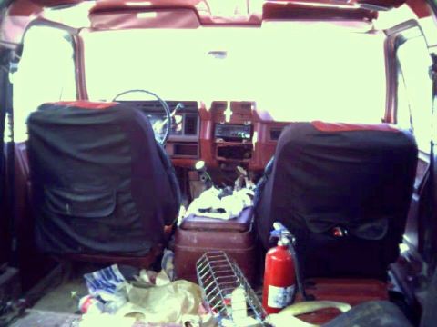 1986 Ford Bronco - The interior of a 1986 Ford Bronco shows its front seats, dashboard, and center console, with items scattered around.