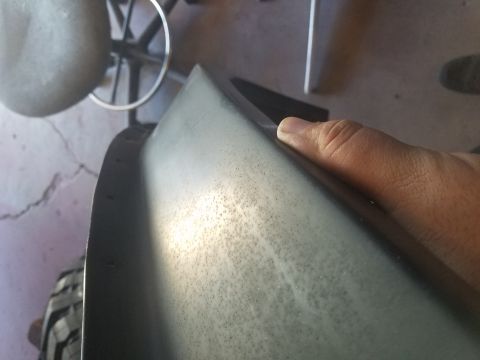 1968 Ford Bronco - A hand is shown resting on the curved, textured surface of a dark gray vehicle fender or body panel. The panel has numerous small, dark spe…