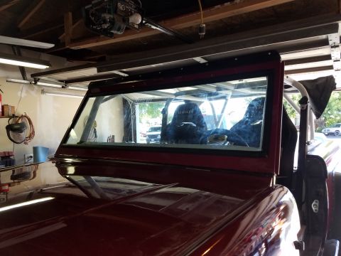 1968 Ford Bronco - A close-up interior view of a red 1968 Ford Bronco shows racing seats and a roll cage. The vehicle is parked inside a garage with a garage…