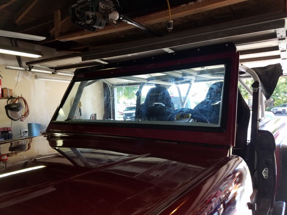 Interior of a red 1968 Ford Bronco with racing seats and roll cage in a garage.