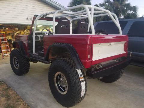 1968 Ford Bronco - A red 1968 Ford Bronco with a white roll cage and racing seats is parked in a driveway next to a garage.