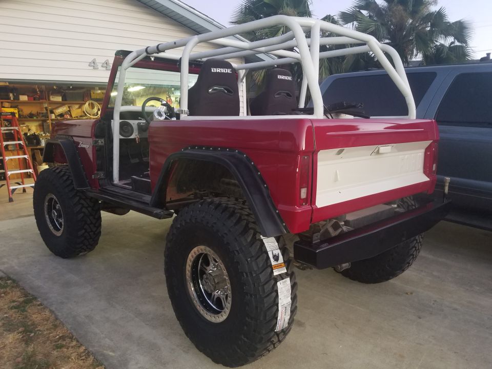 Red 1968 Ford Bronco with white roll cage and racing seats, parked outside a garage.