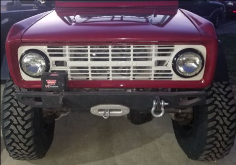 1968 Ford Bronco - Front view of a red Ford Bronco with a white grille, round headlights, and a black bumper with a winch and tow hooks. Large, aggressive off…