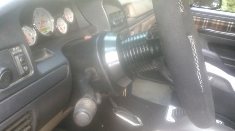 1992 Ford Bronco - Interior close-up looking across the steering column, where a polished steering wheel hub adapter is installed over the black column shroud…