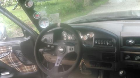 1992 Ford Bronco - Driver's-side interior view of a truck dash showing an aftermarket three-spoke steering wheel with a brushed center hub and slotted spokes…