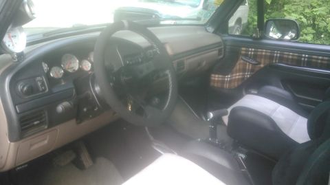 1992 Ford Bronco - Interior of a tan-trimmed 1990s Ford truck/SUV shot from the passenger side, with a fat leather-wrapped steering wheel, a pod of three afte…