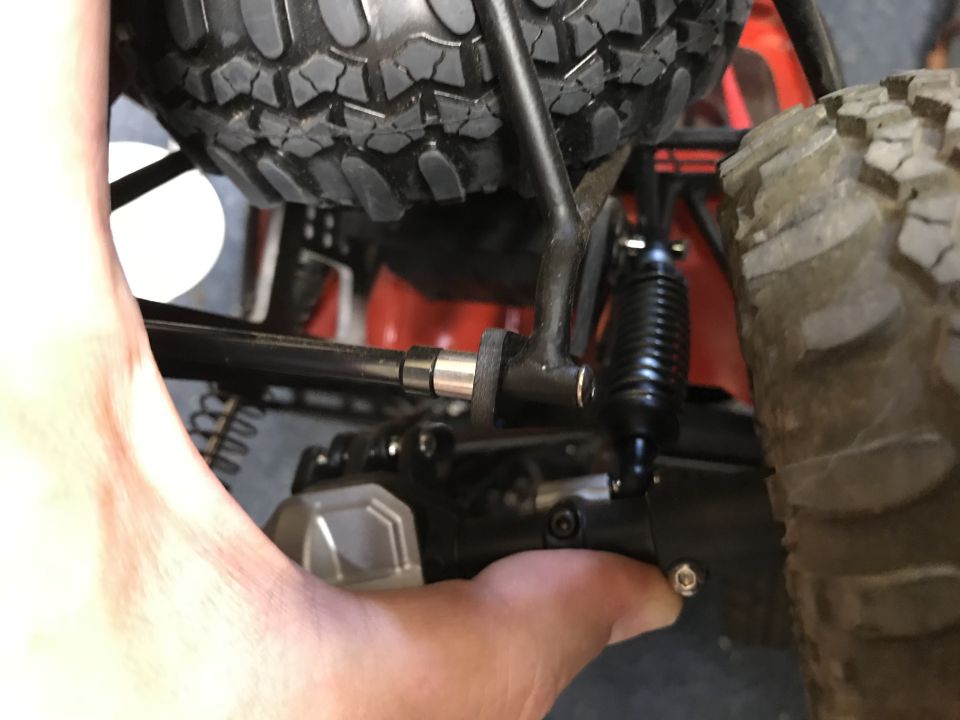 Close-up of RC car suspension, tire, and a hand adjusting a part.