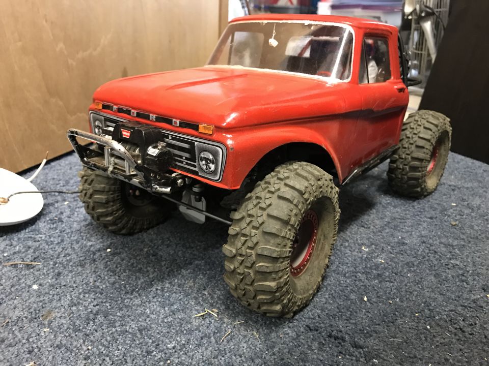 Red RC rock crawler truck with winch and large off-road tires.