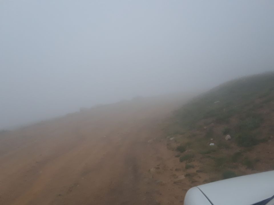 White vehicle part in fog with dirt road and hillside