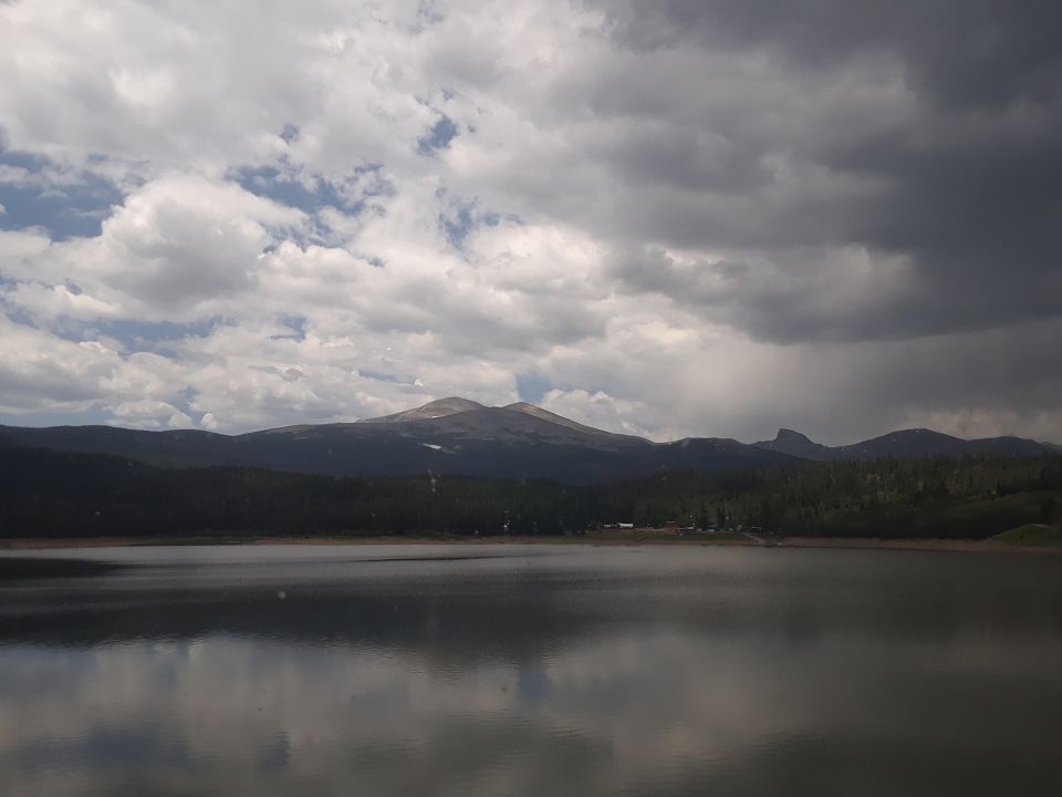 Mountain range reflected in a calm lake under a cloudy sky. Watermark reads SUPERMOTORS