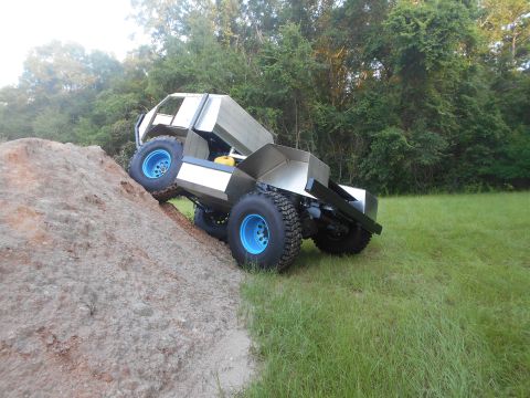 1992 Ford Bronco - A custom-built, silver, four-wheeled vehicle with bright blue rims is shown climbing a dirt embankment. The vehicle has a boxy, utilitarian…