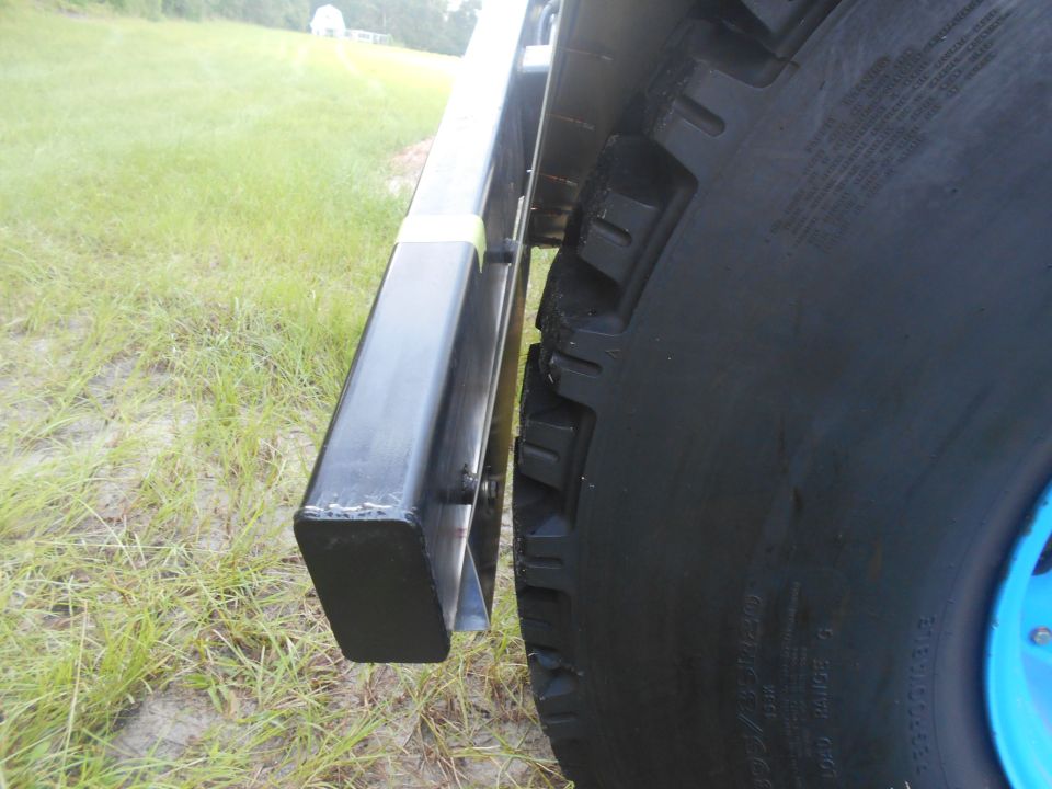 Side view of a large black tire and black metal step on a vehicle parked on grass.