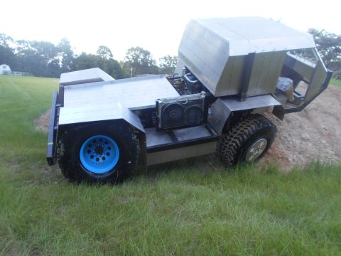 1992 Ford Bronco - A custom-built, open-top vehicle with a silver metallic body is parked on a grassy slope next to a dirt pile. The vehicle features large, o…