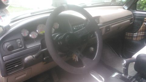 1992 Ford Bronco - Driver's-side interior view of a truck cab with a leather-wrapped steering wheel with white contrast stitching and a bare center hub with n…