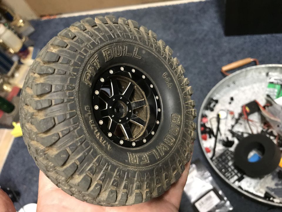 RC car tire with black rim and "PIT BULL GROWLER USA" text, held by a hand.