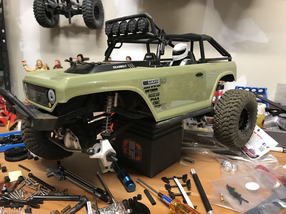 Green RC rock crawler with roll cage and off-road tires on a workbench with tools.