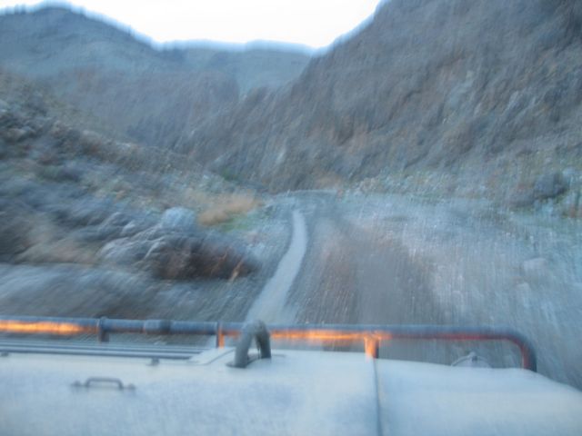 View from inside a vehicle looking out at a winding dirt road through a rocky mountain pass